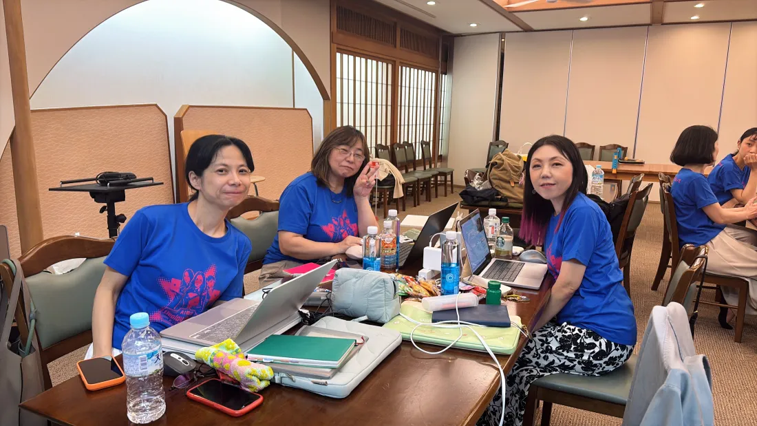 合宿の会場。おそろいのTシャツを着た参加者が、机にノートパソコンを並べて作業している様子